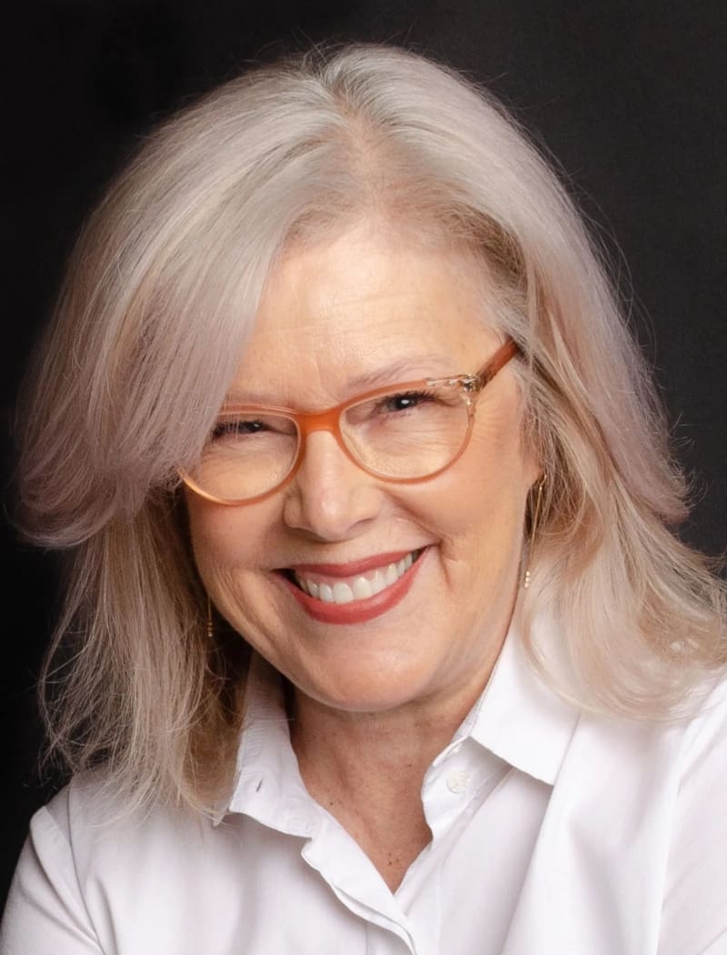 A woman with white hair wearing glasses and smiling.
