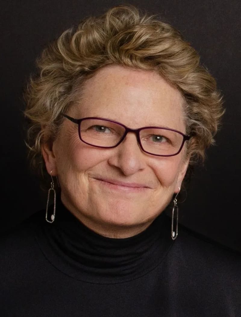 A woman with glasses and short hair wearing black.